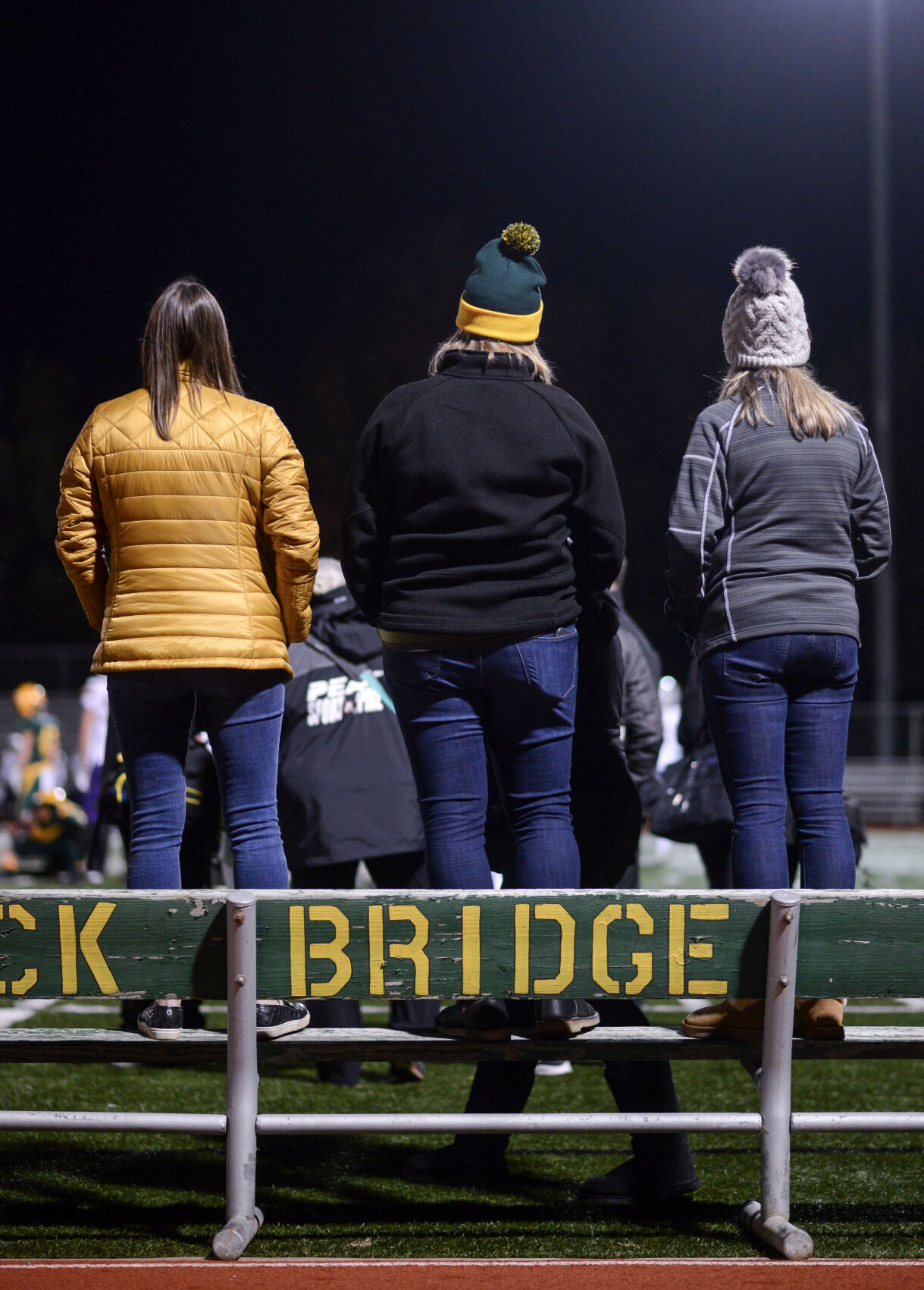 From left, Sarah Messer, Lezlie Norris and Stephanie Dent stand on a bench on the sidelines